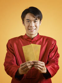 Portrait of man holding cards while standing against orange background