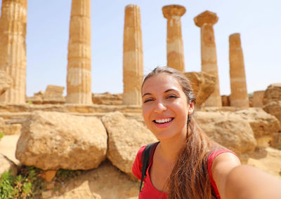 Portrait of smiling young woman against historic columns and sky