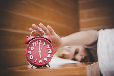 Man pressing alarm clock while sleeping on bed at home