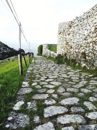 Footpath by wall against sky