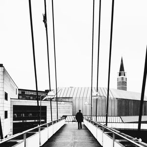 Full length rear view of man walking on bridge in city against clear sky