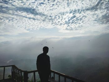 Rear view of silhouette man standing by railing against sky