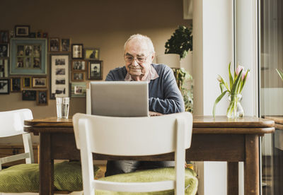 Senior man sitting at table in the living room using laptop