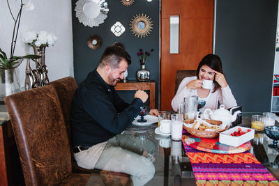 Cheerful young latin american married couple in casual clothes smiling while having breakfast together at home