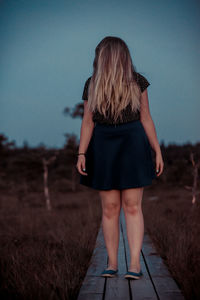 Teenage girl standing on boardwalk against clear sky