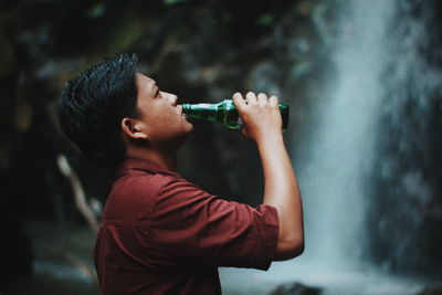 Side view of young man drinking water from bottle