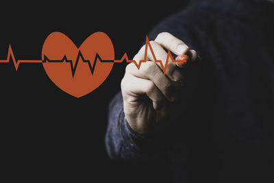 Midsection of man holding heart shape over black background