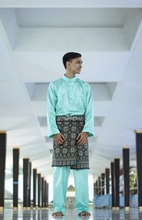 Low angle view of young man in traditional clothing looking away while standing on floor