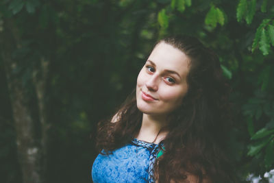 Portrait of beautiful young woman standing against trees