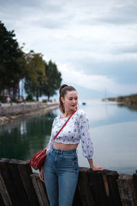 Young woman standing on bridge over lake against sky