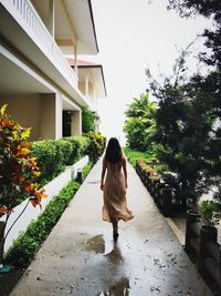 Rear view of woman walking on footpath amidst buildings