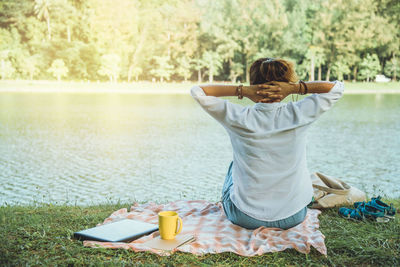 Rear view of woman sitting on grass by water