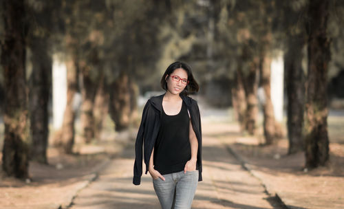 Portrait of woman walking on footpath against trees