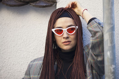 Close-up of thoughtful woman wearing sunglasses against wall