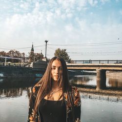 Portrait of young woman standing by bridge against sky