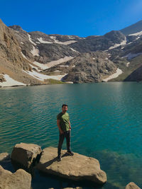 Man standing on rock by lake against sky