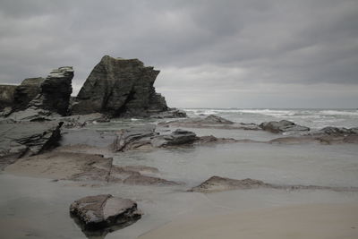 Rock formation on beach against sky