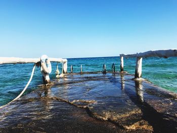 Wooden posts in sea against clear blue sky