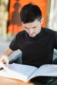 A young man looks through a book menu in a restaurant.