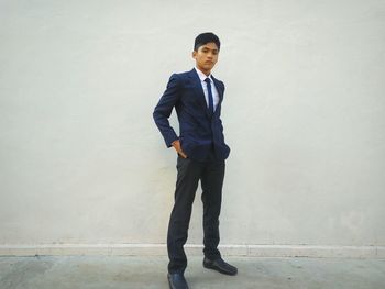 Full length portrait of young businessman standing against wall