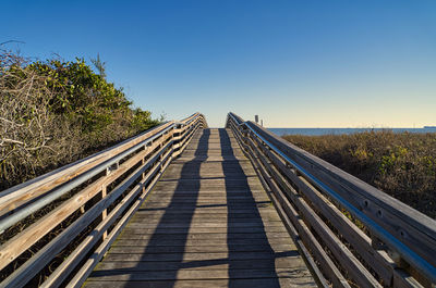 Surface level of footbridge against clear blue sky