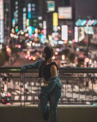 Full length of woman standing against illuminated city at night