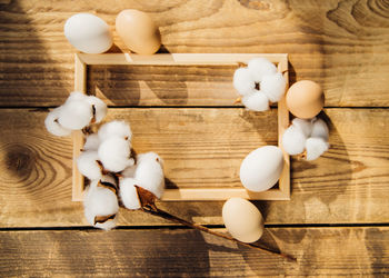 Eggs and a branch with white cotton flowers with sunny shadows on a wooden background.a holiday card