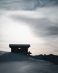 Lifeguard hut on snow covered land against sky during sunrise.