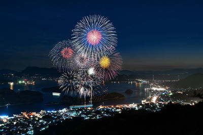 Firework display over illuminated city against sky at night