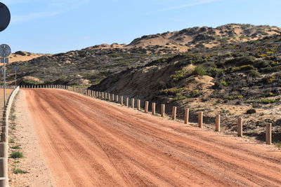 Dirt road by mountain against sky