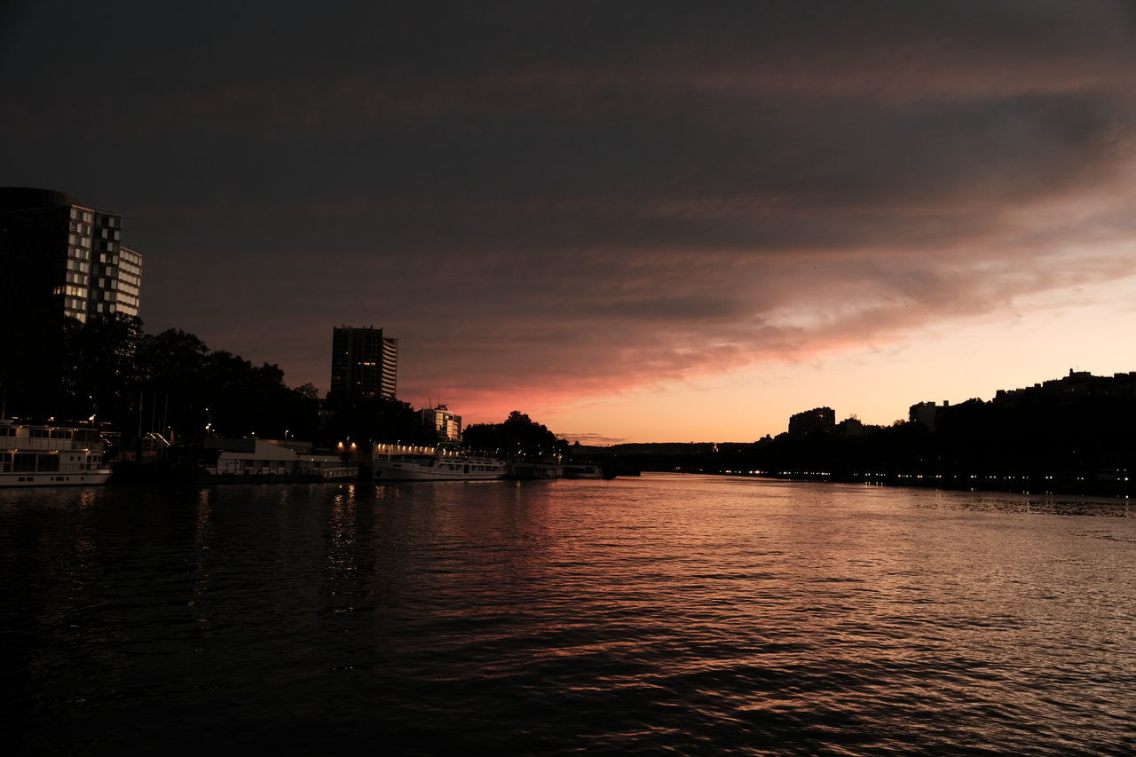 SCENIC VIEW OF RIVER BY BUILDINGS AGAINST SKY DURING SUNSET