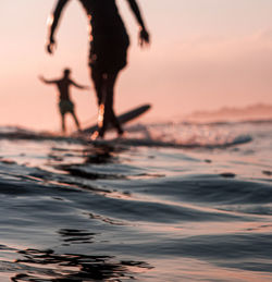 Low section of silhouette people on beach against sky during sunset