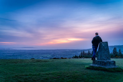 Rear view of man standing on field against sky during sunset