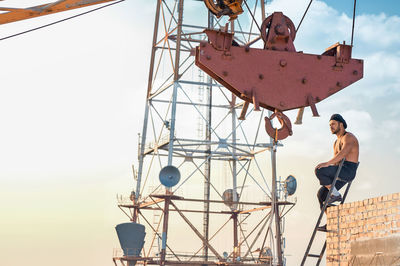 Low angle view of man standing on ladder against sky