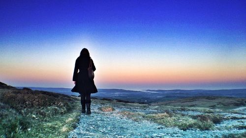 Silhouette of woman standing on landscape at sunset