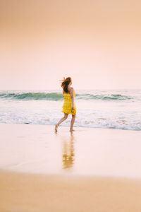 Woman walking at beach against sea against sky