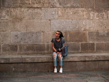 Full length of teenage girl sitting against wall