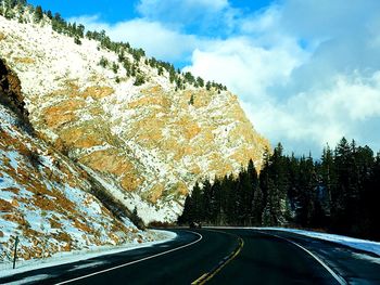 Road amidst trees and snowcapped mountains against sky