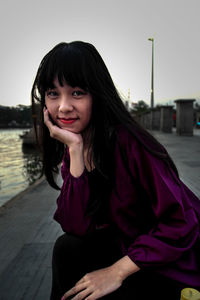 Portrait of smiling young woman sitting against sky