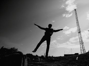 Silhouette man with arms outstretched posing on field against sky