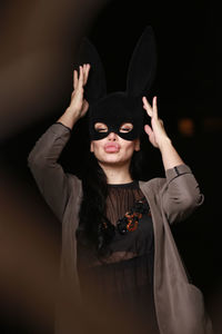 Woman wearing mask making face against black background