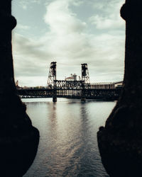 Silhouette of bridge over river against cloudy sky