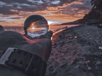 Midsection of man holding camera against sky during sunset