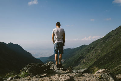 Rear view of man standing on mountain against sky