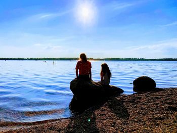 Rear view of woman sitting by lake against sky
