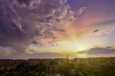 Buildings in city against dramatic sky during sunset