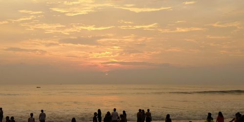 Silhouette people on beach against sky during sunset