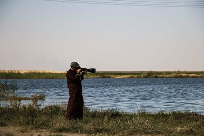 Man photographing on lake against sky