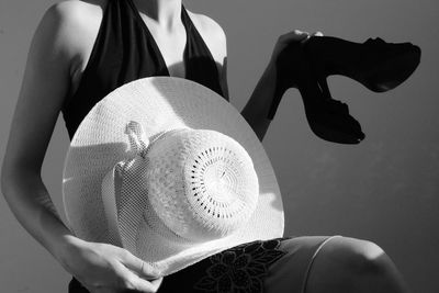 Midsection of woman with hat and shoes sitting against wall