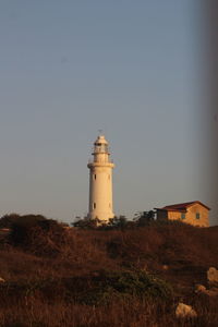 Lighthouse on field by building against clear sky